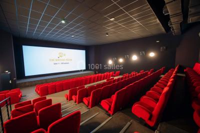 Salle de cinéma vide avec des rangées de sièges rouges et un grand écran allumé affichant un logo et du texte.