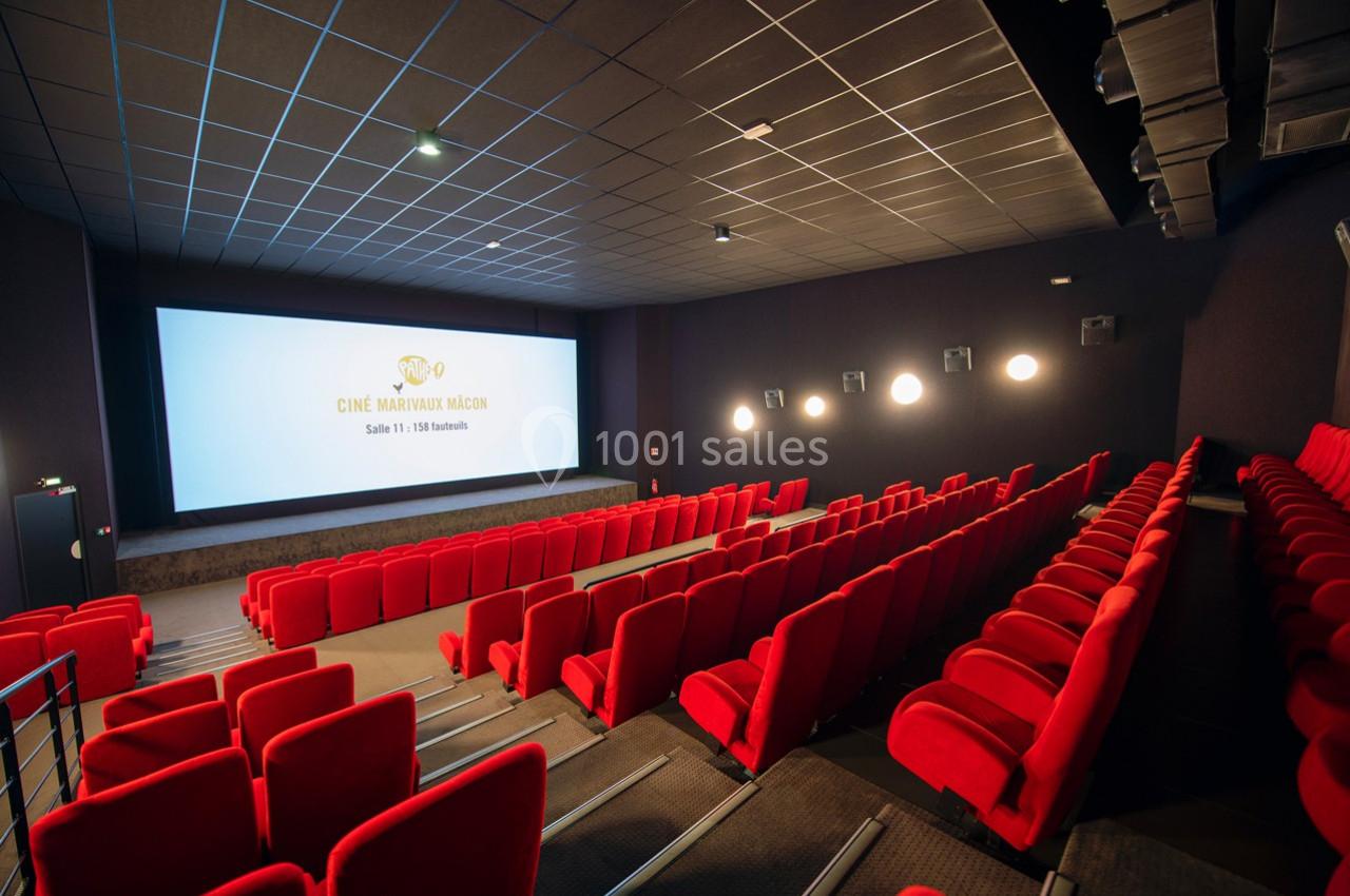 Salle de cinéma vide avec des rangées de sièges rouges et un grand écran allumé affichant un logo et du texte.