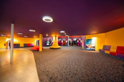Salle de cinéma vide avec des rangées de sièges rouges et un grand écran allumé affichant un logo et du texte.