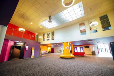 Salle de cinéma vide avec des rangées de sièges rouges et un grand écran allumé affichant un logo et du texte.