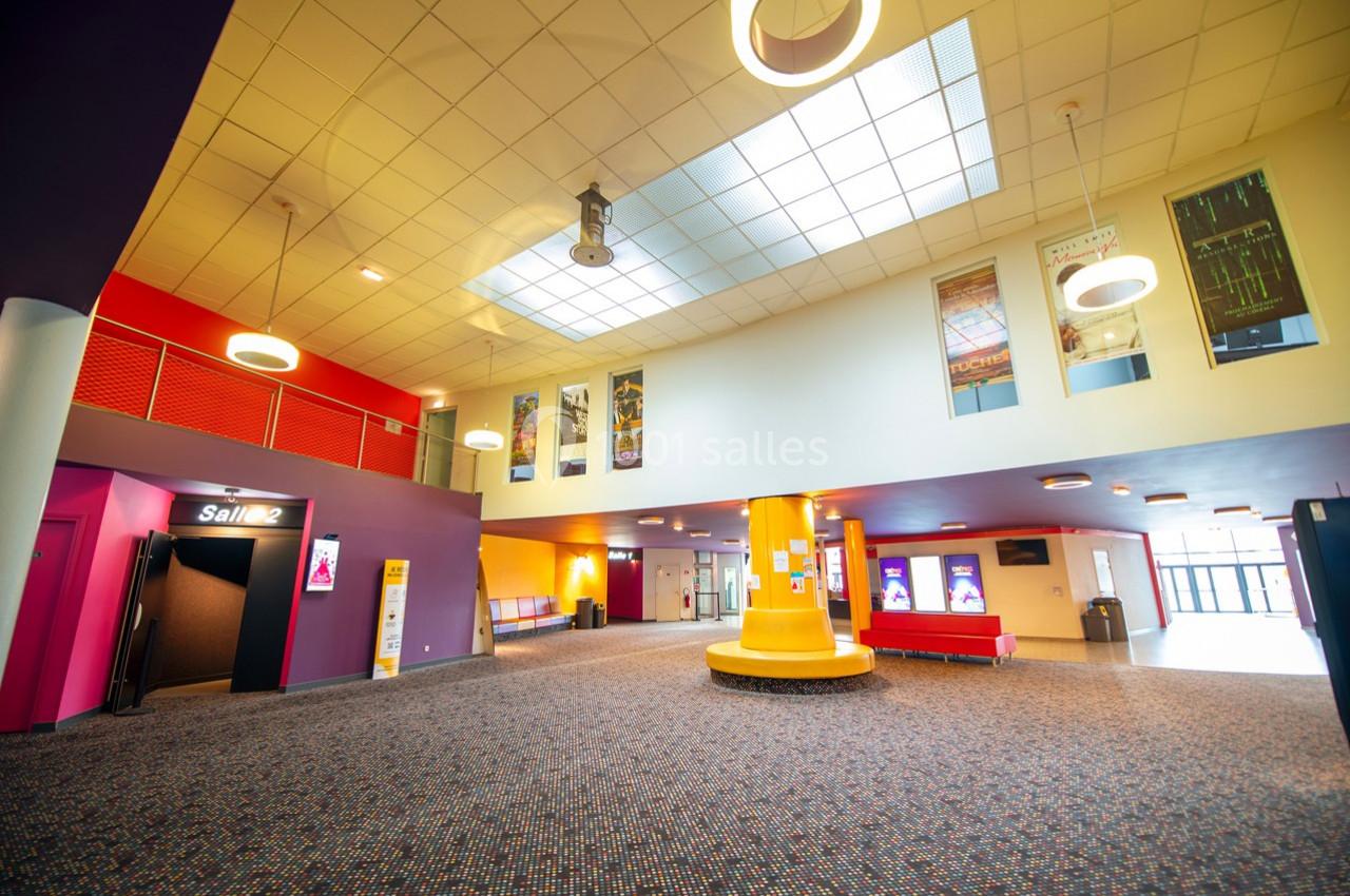Hall spacieux d'un cinéma avec éclairage moderne, affiches de films, entrée de salle et guichet visibles.
