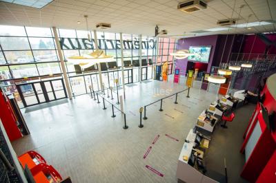 Salle de cinéma vide avec des rangées de sièges rouges et un grand écran allumé affichant un logo et du texte.