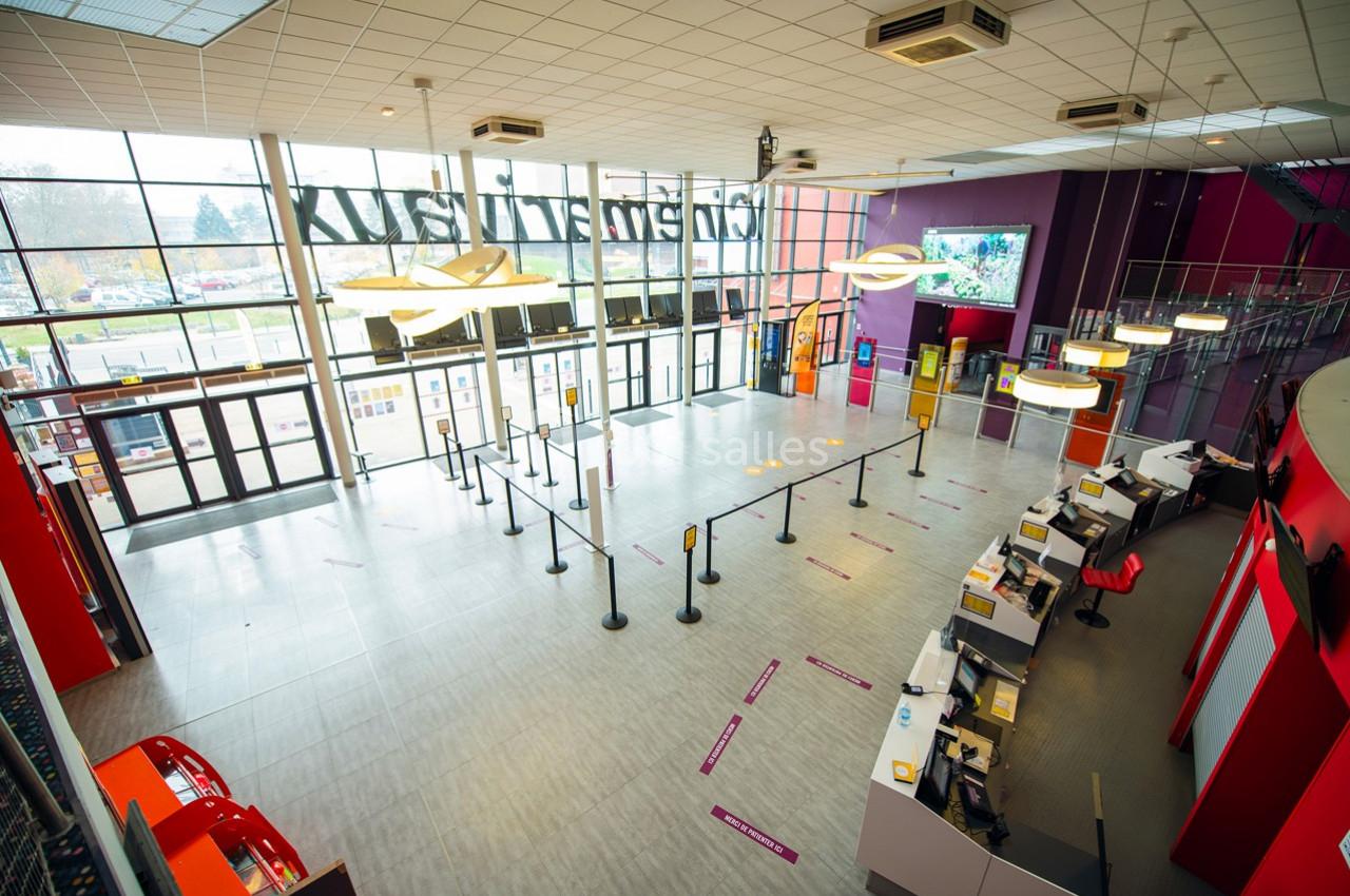 Hall d'entrée spacieux avec guichets, files d'attente délimitées et grandes baies vitrées donnant sur l'extérieur.