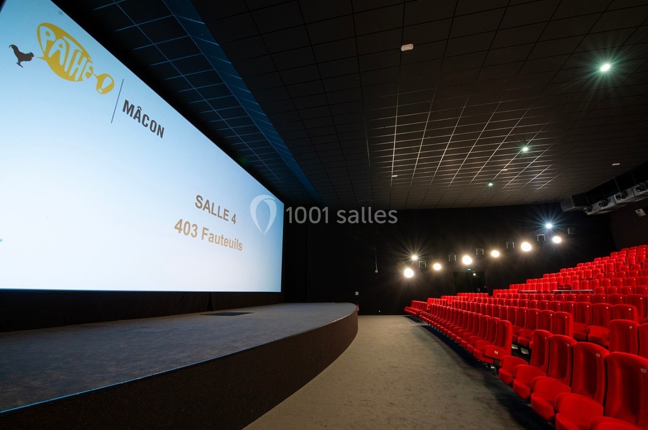 Salle de cinéma moderne avec écran géant, rangées de fauteuils rouges et éclairage tamisé.