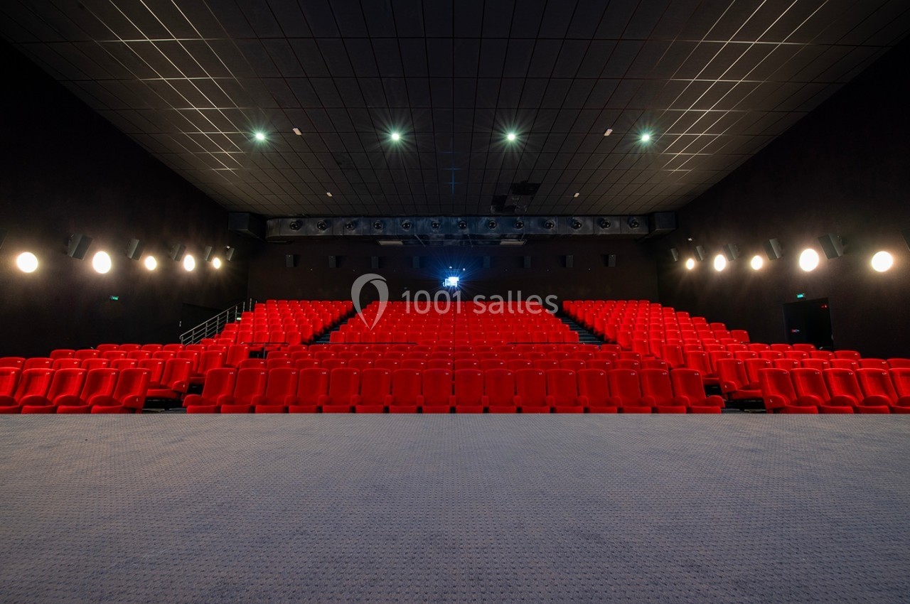 Salle de cinéma vide avec des rangées de sièges rouges, éclairage tamisé et écran éteint au fond.