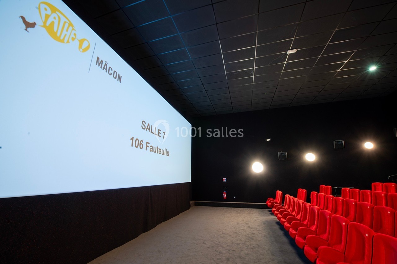 Salle de cinéma avec écran allumé, rangées de fauteuils rouges et éclairage mural discret.