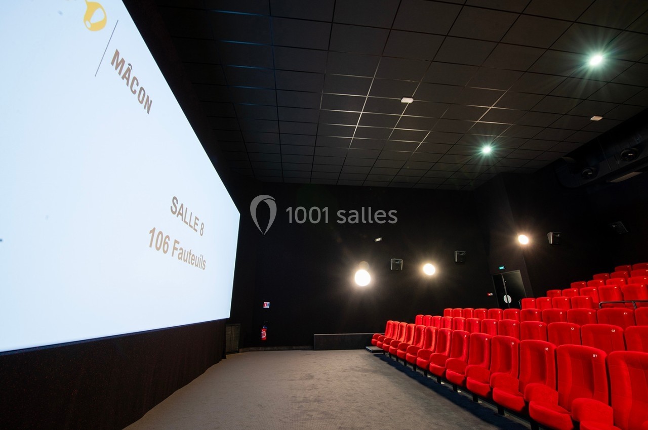 Salle de cinéma avec rangées de sièges rouges, écran blanc affichant ’Salle 8 - 106 fauteuils’ et éclairage tamisé.