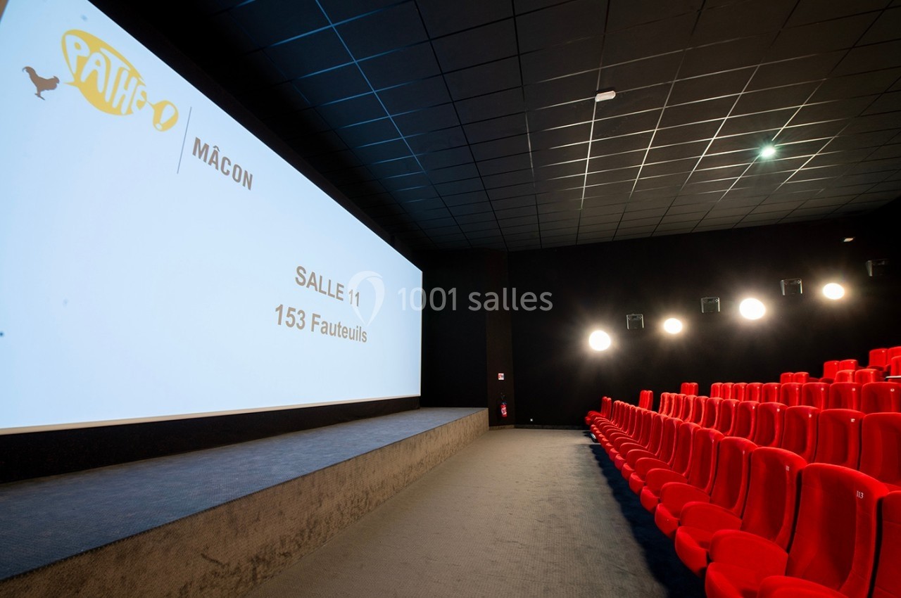 Salle de cinéma avec écran blanc, rangées de fauteuils rouges et éclairage mural discret.