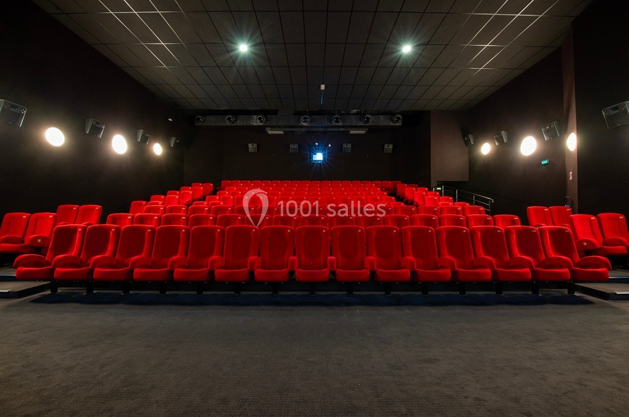 Salle de cinéma vide avec des rangées de sièges rouges et un écran éteint en arrière-plan.