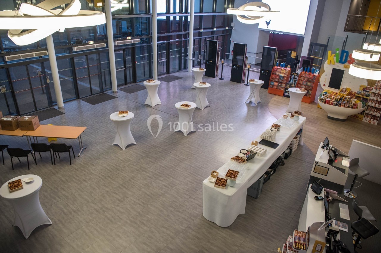 Vue d'une salle d'accueil moderne avec des tables hautes dressées et un comptoir de service.