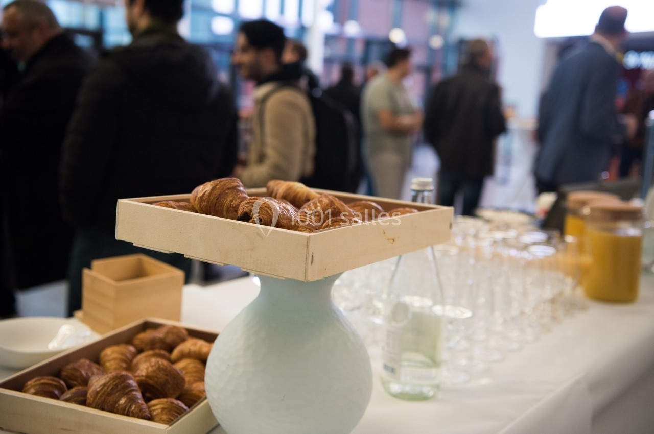 Plateau de croissants sur une table dressée avec des boissons et des verres, dans un espace avec des personnes en arrière…