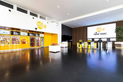 Façade d'un cinéma moderne avec enseigne IMAX, éclairée en soirée, entourée de végétation et d'un parking.