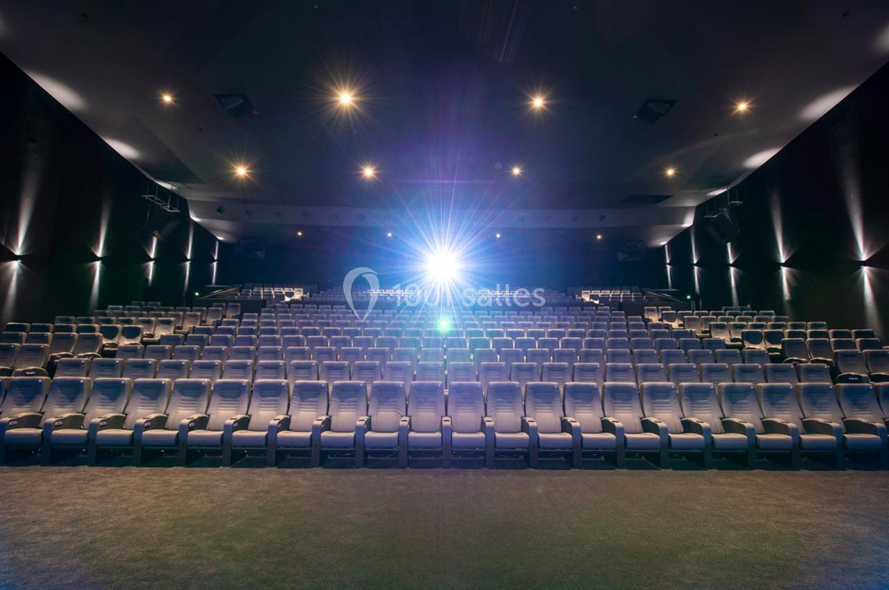 Salle de cinéma vide avec des rangées de sièges alignés et un projecteur allumé au fond.