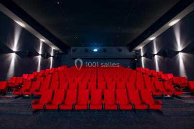 Façade d'un cinéma avec un parking au premier plan, quelques arbres et un ciel dégagé en arrière-plan.