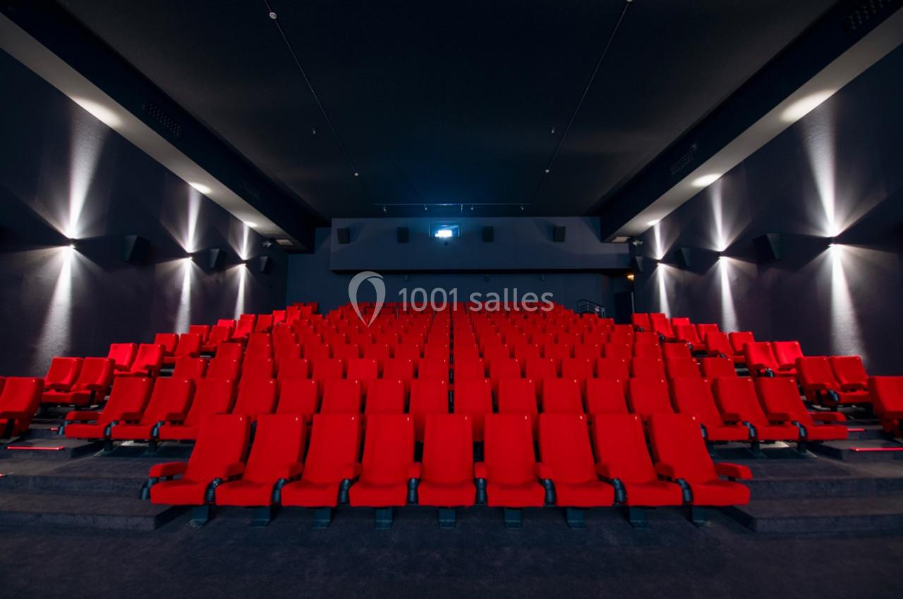 Salle de cinéma vide avec des rangées de sièges rouges et un écran blanc en arrière-plan.
