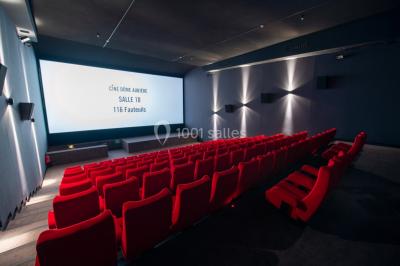 Façade d'un cinéma avec un parking au premier plan, quelques arbres et un ciel dégagé en arrière-plan.