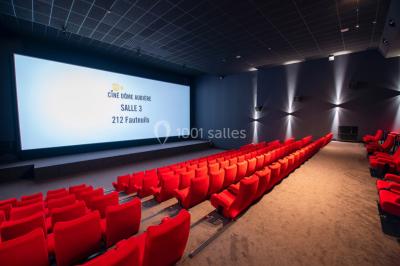 Façade d'un cinéma avec un parking au premier plan, quelques arbres et un ciel dégagé en arrière-plan.