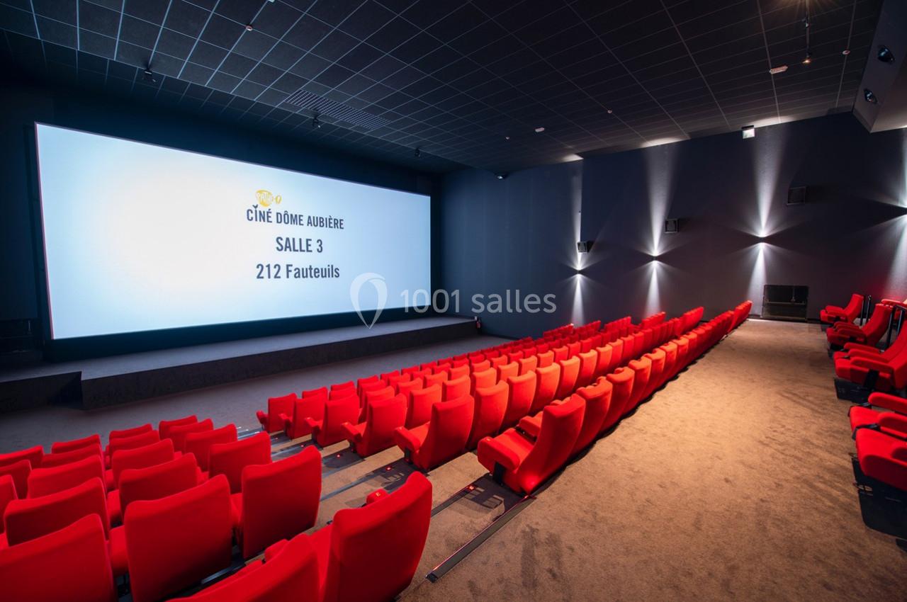 Salle de cinéma moderne avec rangées de fauteuils rouges, écran géant allumé et éclairage tamisé.