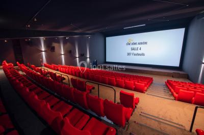 Façade d'un cinéma avec un parking au premier plan, quelques arbres et un ciel dégagé en arrière-plan.