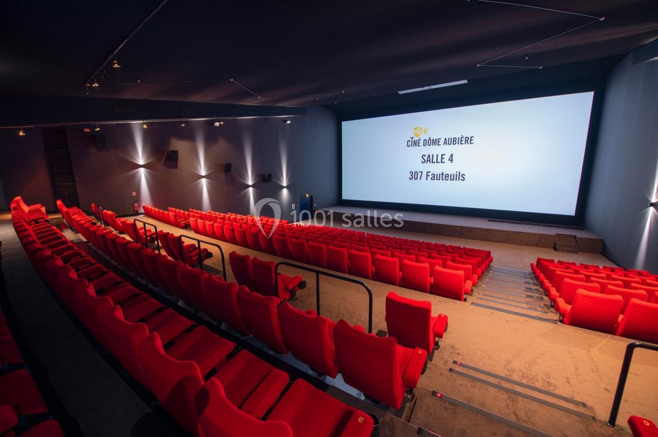 Salle de cinéma vide avec des sièges rouges, écran géant et éclairage tamisé.