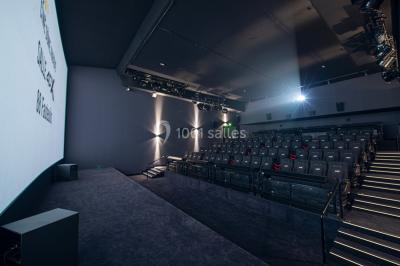 Façade d'un cinéma avec un parking au premier plan, quelques arbres et un ciel dégagé en arrière-plan.