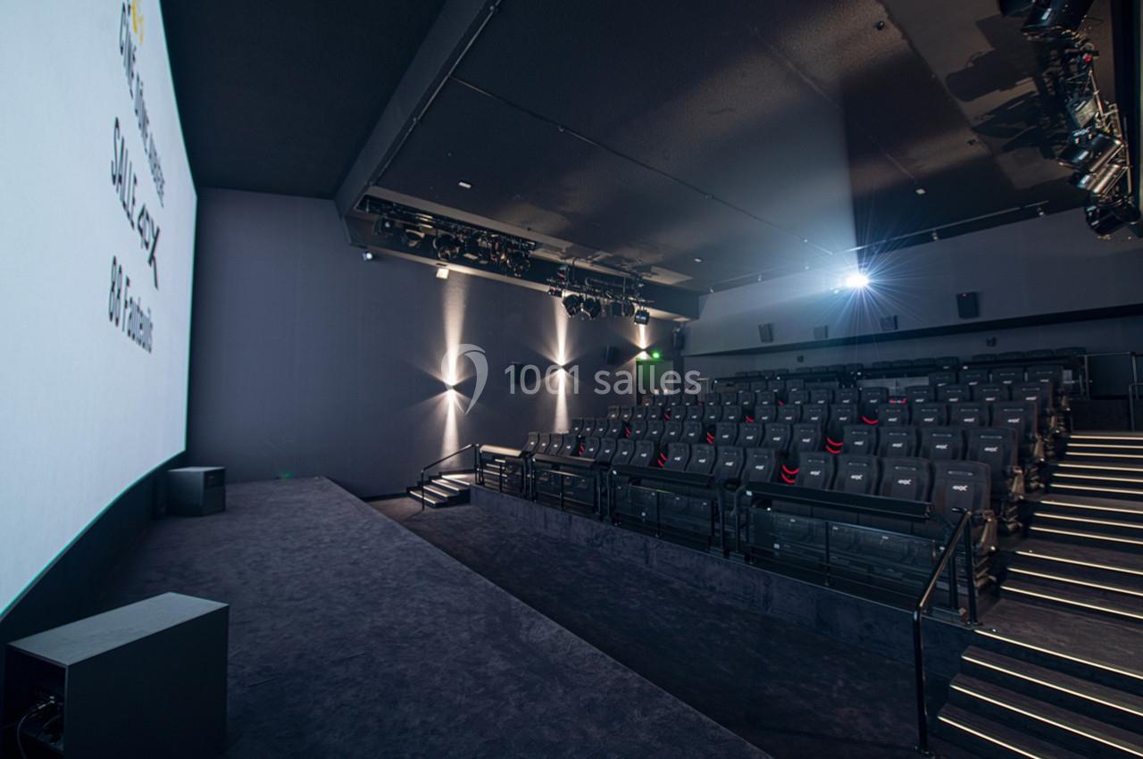Salle de cinéma moderne avec sièges vides, écran blanc allumé et éclairage tamisé.