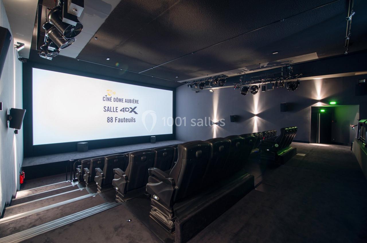 Salle de cinéma moderne avec écran allumé, sièges inclinables et éclairage tamisé.