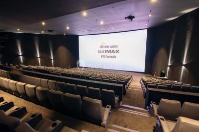 Façade d'un cinéma avec un parking au premier plan, quelques arbres et un ciel dégagé en arrière-plan.