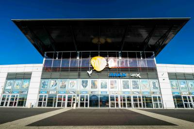 Façade d'un cinéma avec un parking au premier plan, quelques arbres et un ciel dégagé en arrière-plan.