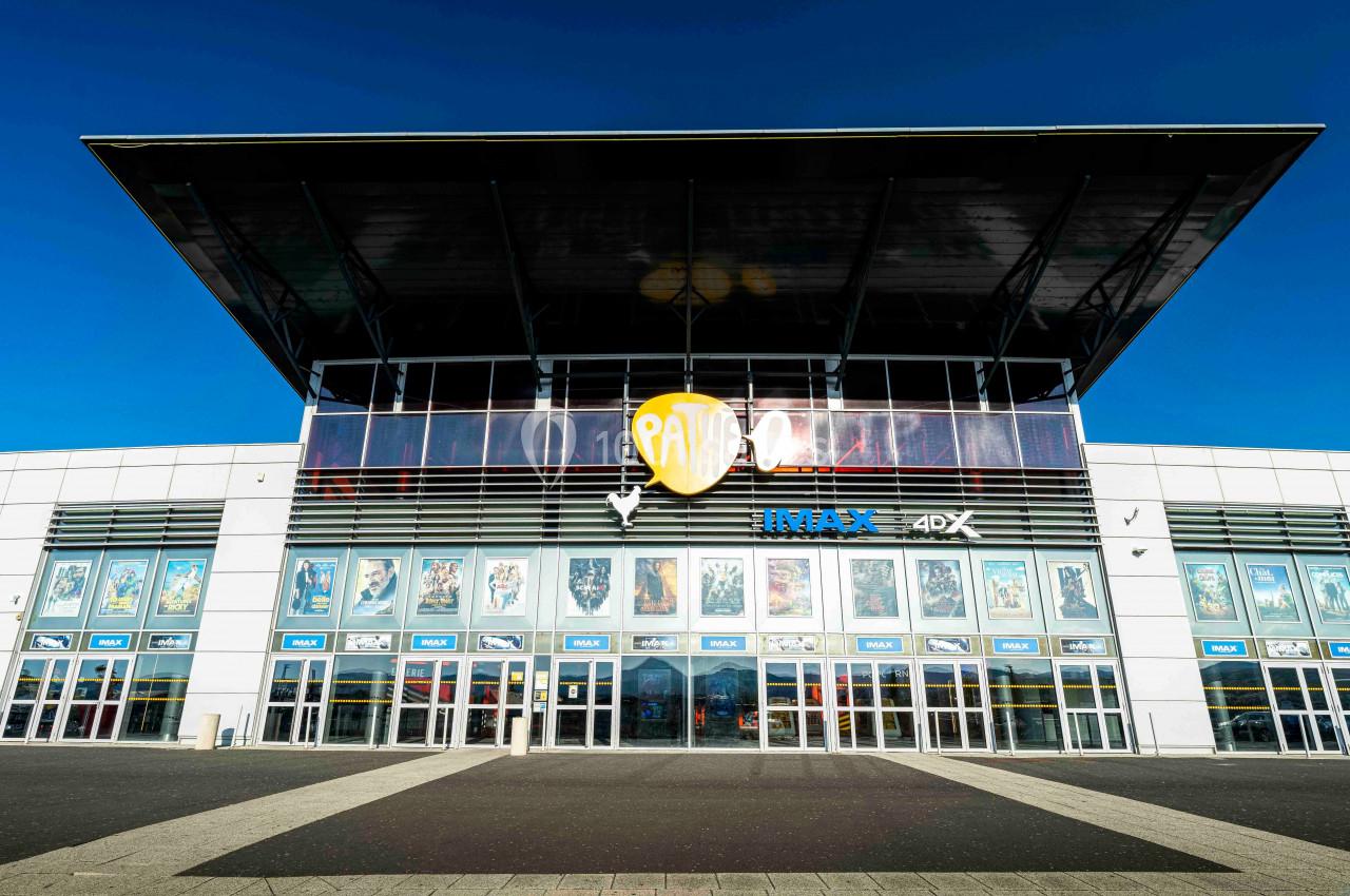 Façade d'un cinéma moderne avec affiches de films visibles sur les vitrines et un grand logo central.