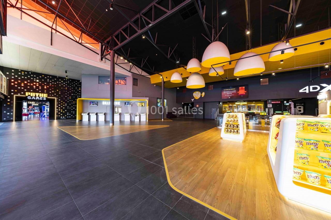 Hall spacieux d'un cinéma avec comptoirs de billetterie, éclairage moderne et présentoirs de confiseries.