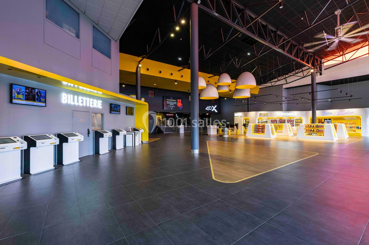 Hall de cinéma moderne avec bornes de billetterie, comptoirs lumineux et signalétique pour une salle 4DX.