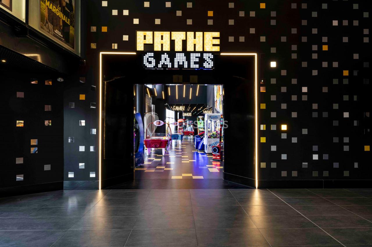 Entrée d'une salle d'arcade lumineuse avec enseigne ’Pathé Games’ et jeux visibles à l'intérieur.