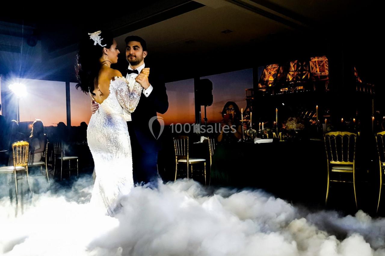 Un couple danse sur une piste entourée de fumée, avec une vue nocturne et la Tour Eiffel en arrière-plan.