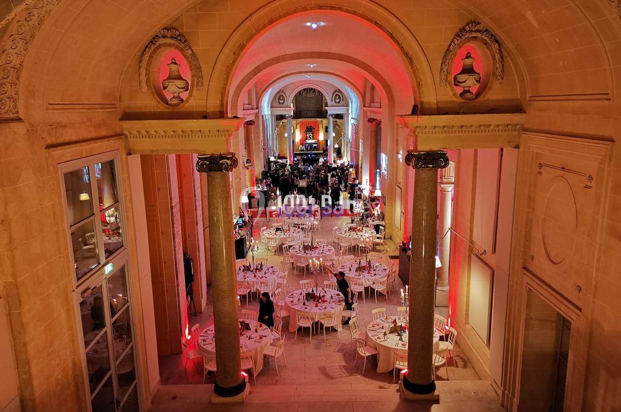 Salle de réception élégante avec tables rondes dressées, éclairage chaleureux et architecture classique.