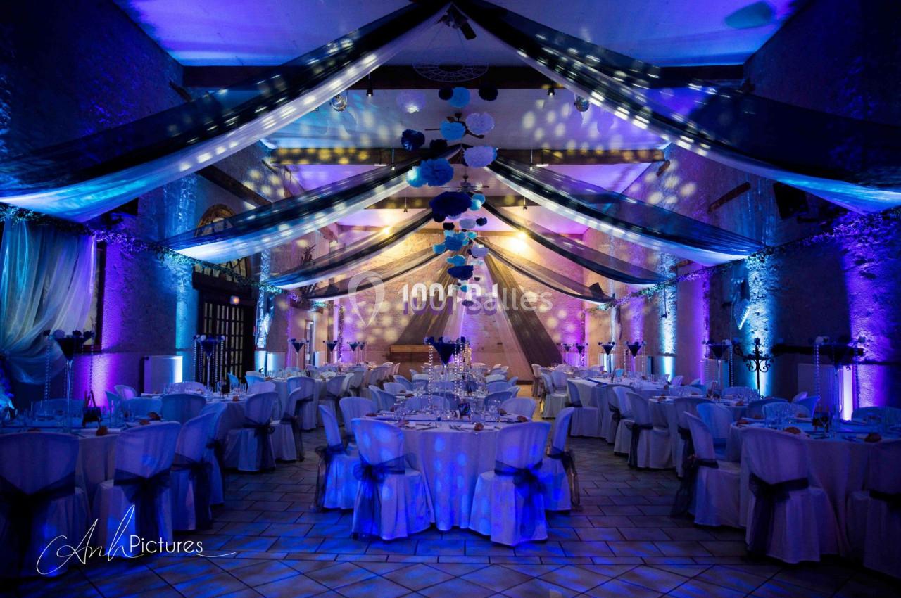 Salle de réception décorée avec des tables dressées, éclairages colorés et guirlandes suspendues au plafond.