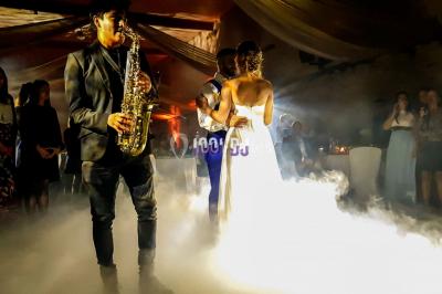 Un couple danse au milieu d'une piste entourée de fumée, tandis qu'un musicien joue du saxophone en avant-plan.