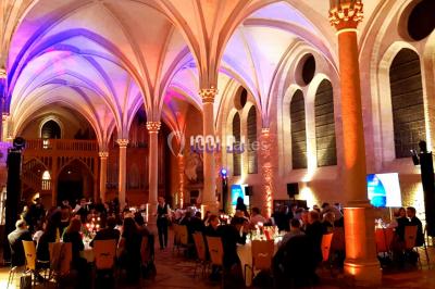 Vue d'une régie DJ avec platines et ordinateur, face à une salle éclairée en violet lors d'un événement festif.