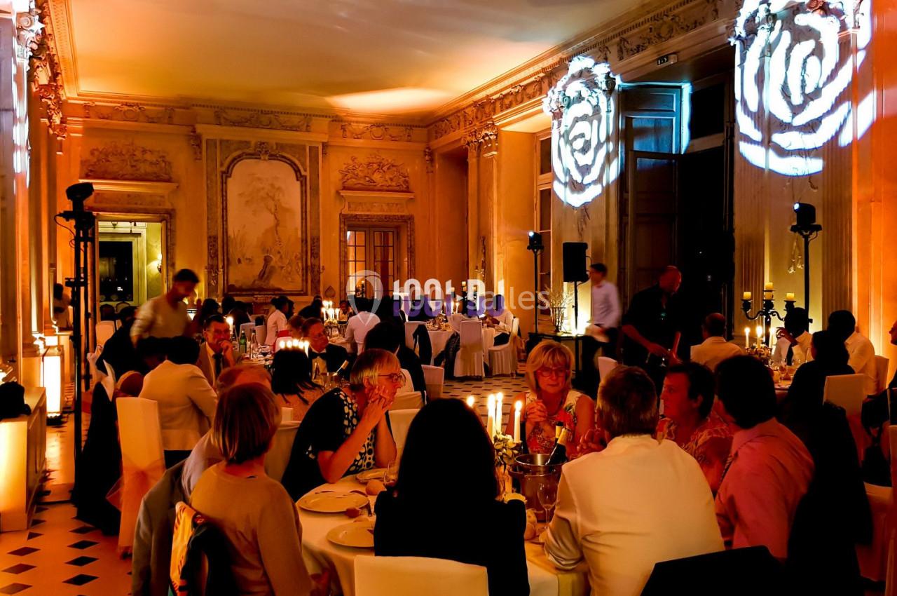 Salle élégante avec des convives dînant à des tables décorées, éclairage tamisé et projections lumineuses sur les murs.