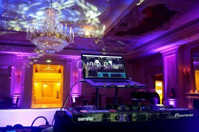 Vue d'une régie DJ avec platines et ordinateur, face à une salle éclairée en violet lors d'un événement festif.