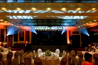 Vue d'une régie DJ avec platines et ordinateur, face à une salle éclairée en violet lors d'un événement festif.
