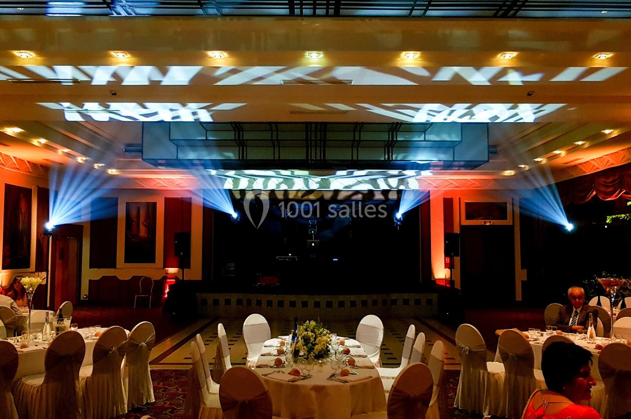 Salle de réception décorée avec des tables dressées, éclairages colorés et projecteurs illuminant le plafond.