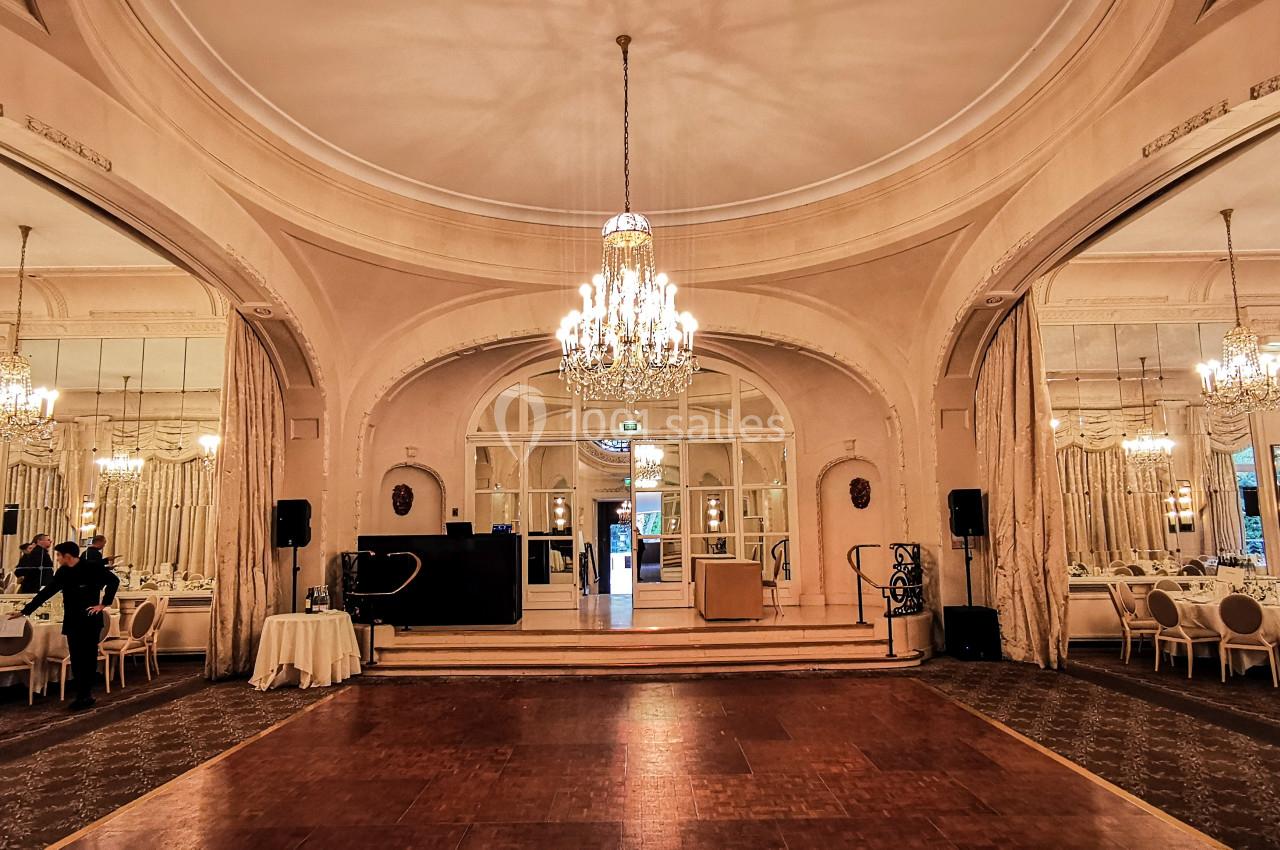 Salle de réception élégante avec lustres, miroirs et tables dressées, prête pour un événement.