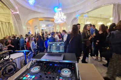 Vue d'une régie DJ avec platines et ordinateur, face à une salle éclairée en violet lors d'un événement festif.