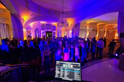 Vue d'une régie DJ avec platines et ordinateur, face à une salle éclairée en violet lors d'un événement festif.