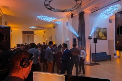 Vue d'une régie DJ avec platines et ordinateur, face à une salle éclairée en violet lors d'un événement festif.