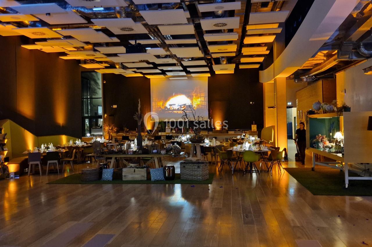 Salle de réception éclairée en tons chauds, avec tables dressées, décorations et plafond au design moderne.