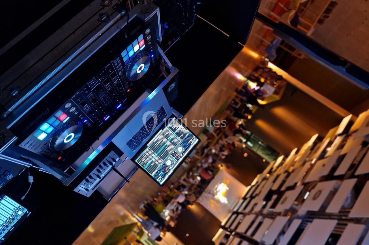 Table de mixage avec ordinateur affichant des logiciels audio, installée dans un espace intérieur animé en arrière-plan.