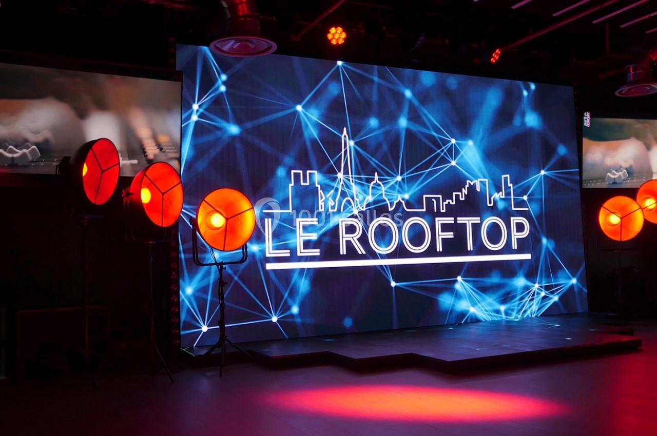 Écran lumineux affichant ’Le Rooftop’ avec des projecteurs orange dans une salle sombre.