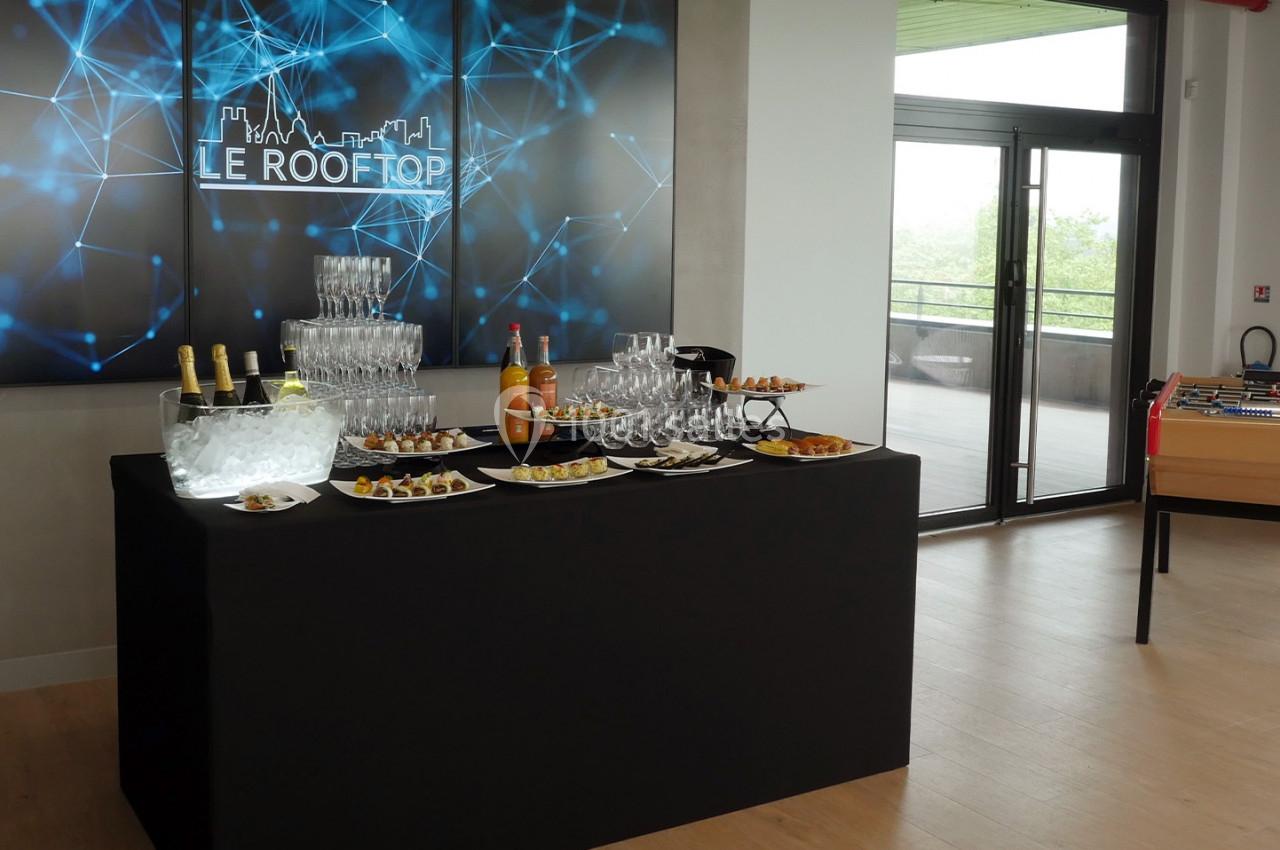 Buffet avec boissons, verrines et amuse-bouches dans une salle moderne avec baby-foot et vue sur une terrasse.